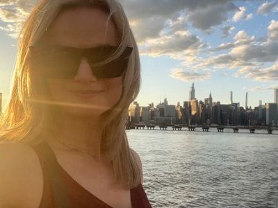 Lauren Buglioli is taking a selfie with the shades on and buildings in the background.